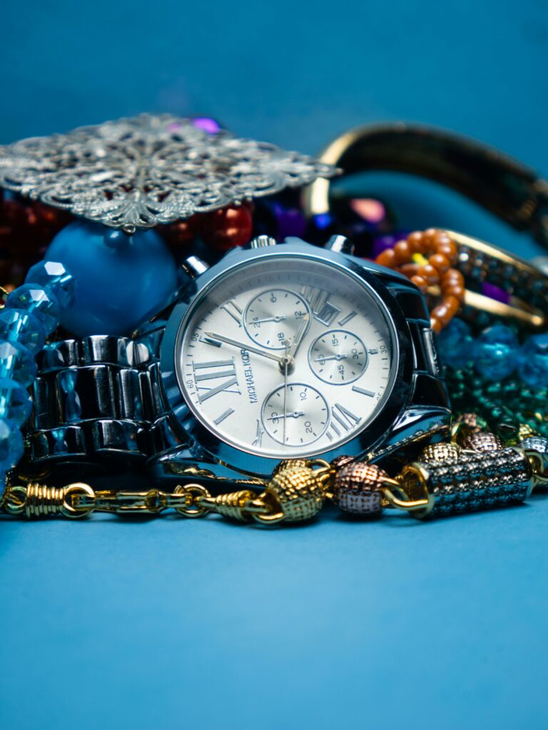 Close-up of a luxury wristwatch surrounded by colorful jewelry against a blue surface.