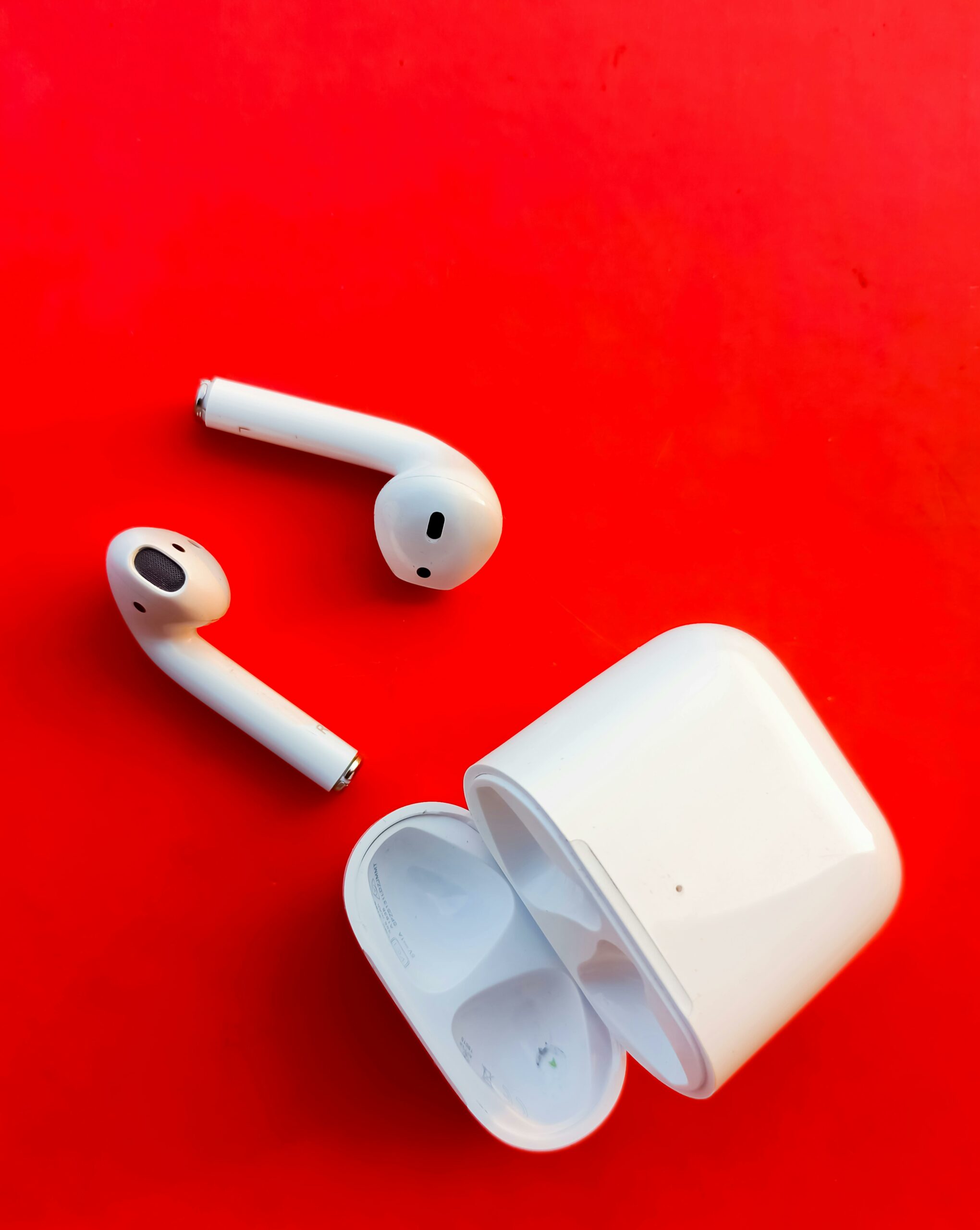 Home White wireless earbuds and charging case on a striking red backdrop, highlighting modern audio technology.